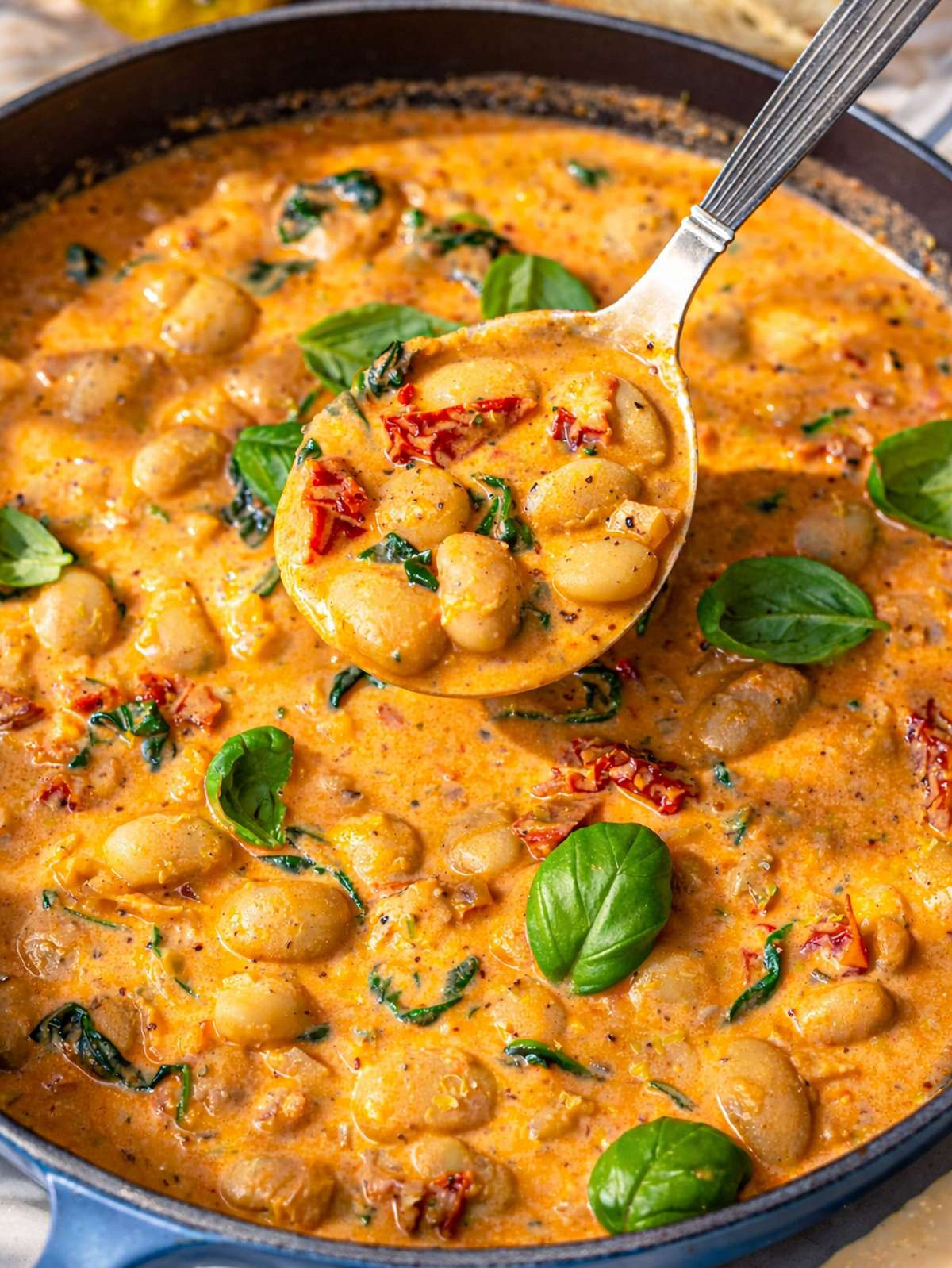 Close-up of velvety sun-dried tomato sauce coating large butter beans and wilted spinach.