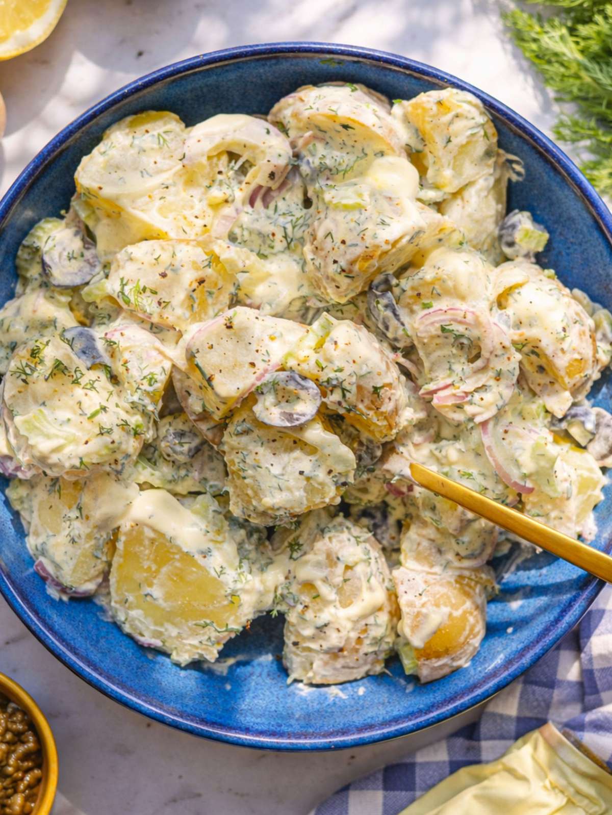 Creamy Greek yogurt potato salad in a bowl with herbs and olives.