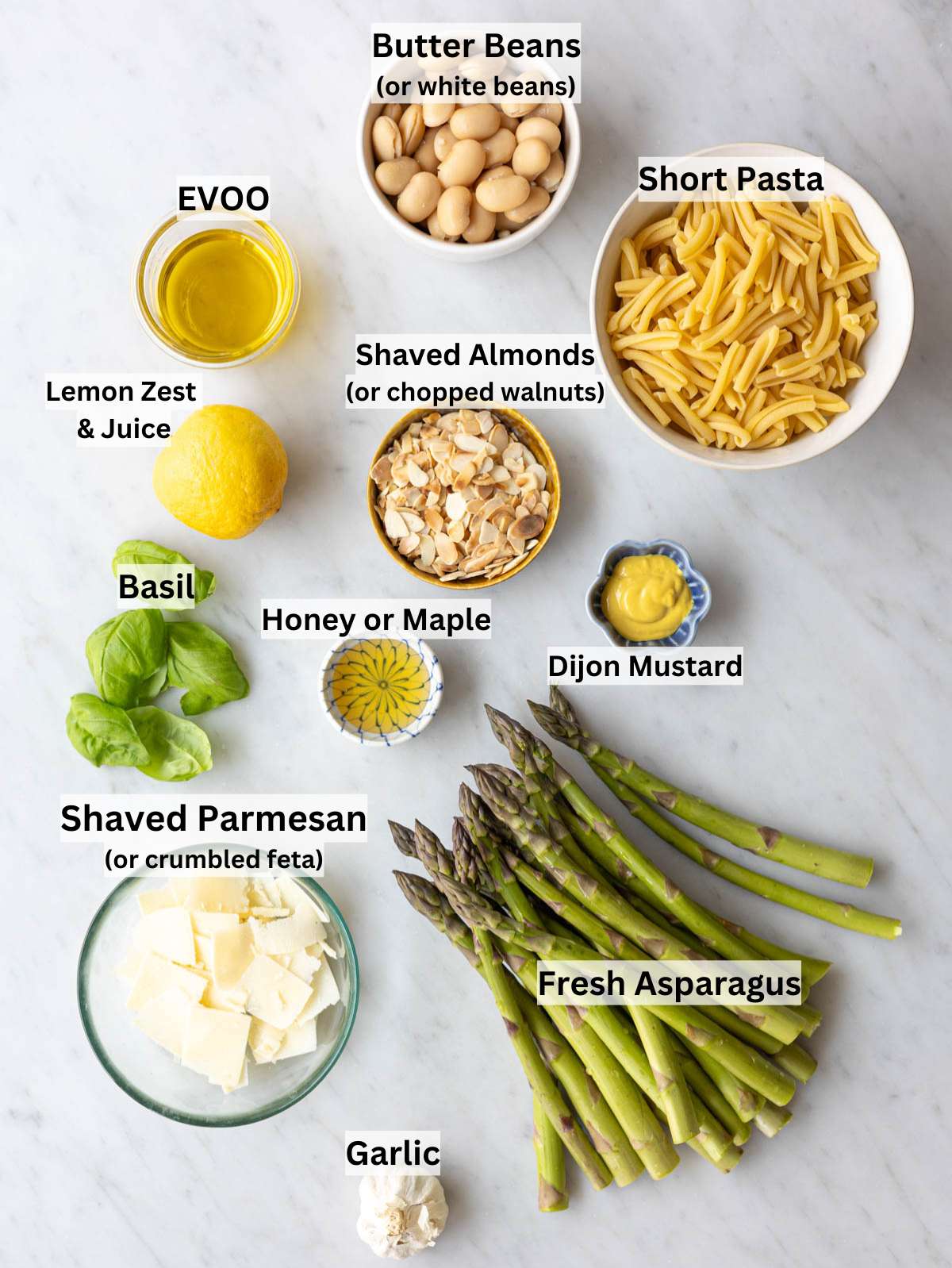 Fresh asparagus spears, white butter beans, and lemons on a bright white marble surface.