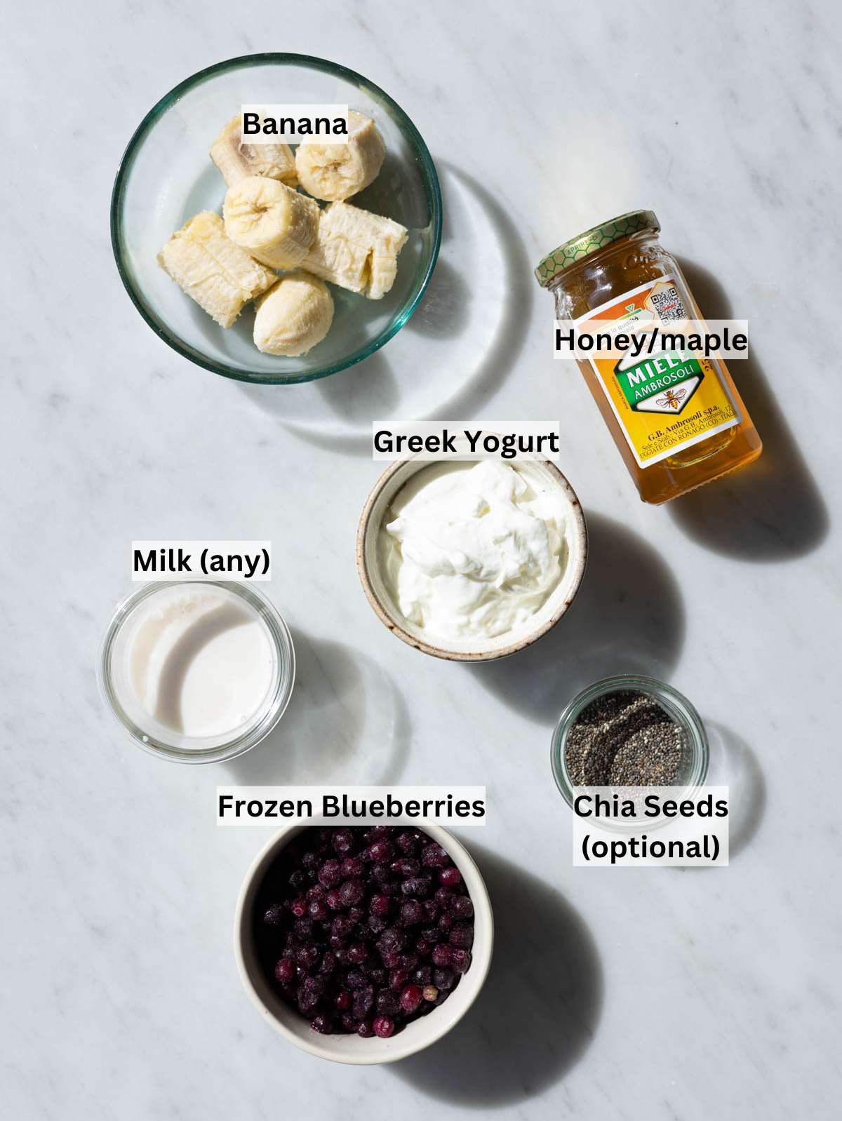 Fresh blueberries, a sliced banana, Greek yogurt, and chia seeds arranged on a bright marble surface.