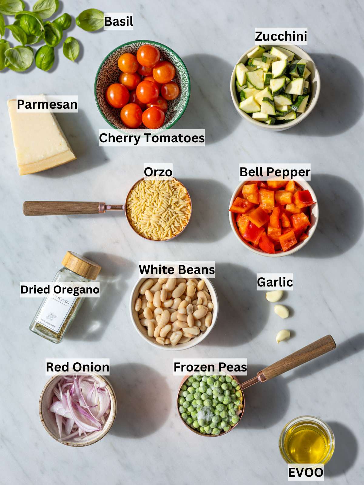 Fresh vegetables, orzo, beans, and herbs arranged on marble surface in soft window light.