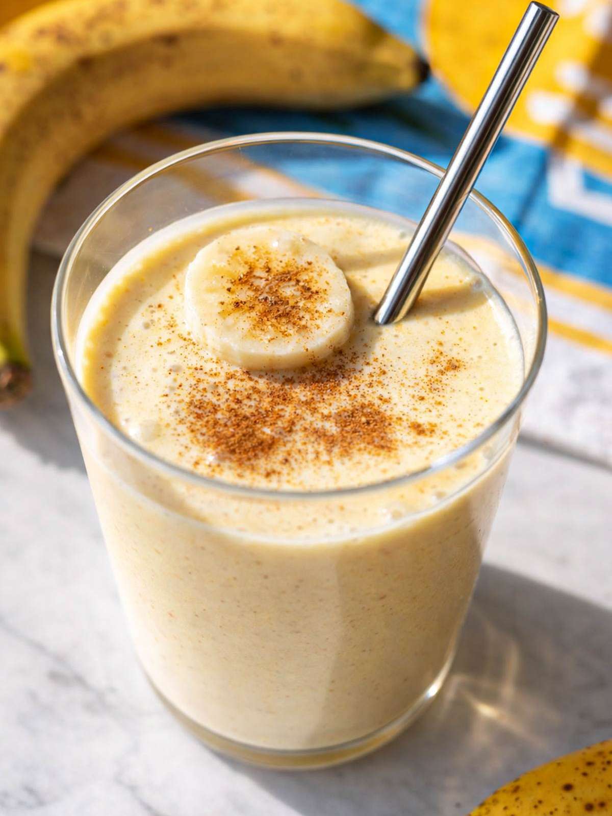 Glass of Greek Yogurt Banana Smoothie on marble surface near bright window.