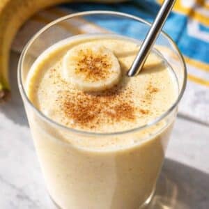Greek Yogurt Banana Smoothie in tall glass with sliced banana on marble table.