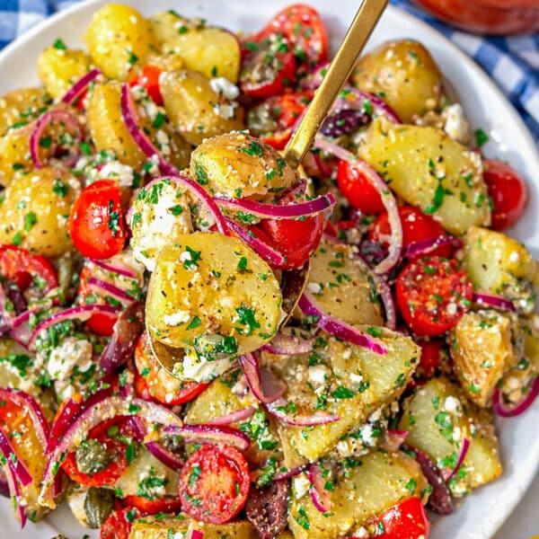 Greek potato salad on marble table with bright tomatoes olives capers and feta.