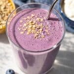 Greek yogurt breakfast smoothie in tall glass with blueberries on marble surface in soft natural light.