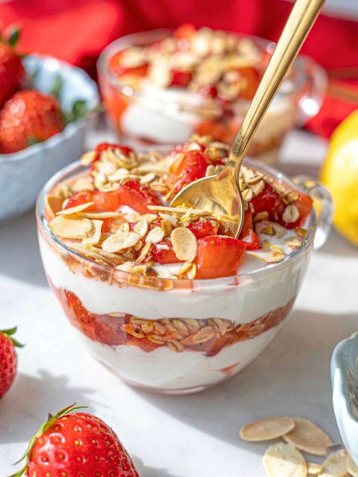 Greek yogurt parfait layered with strawberries and crunchy topping in glass cup.