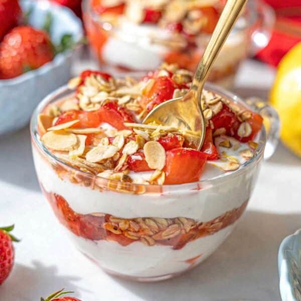 Greek yogurt parfait with strawberries in glass cup, soft natural light on marble.