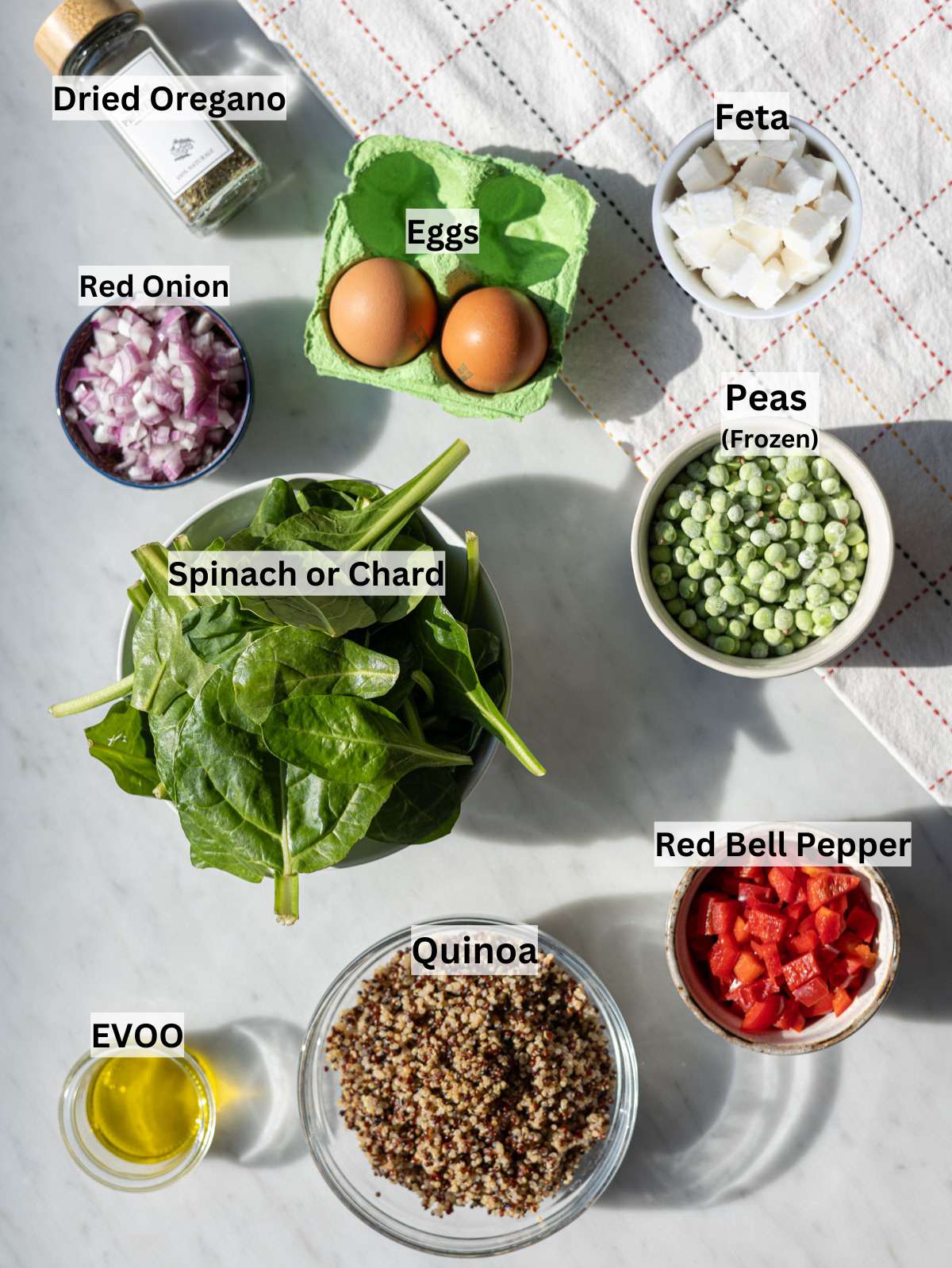 Ingredients arranged on marble table with quinoa eggs spinach peas and bell pepper in natural light.