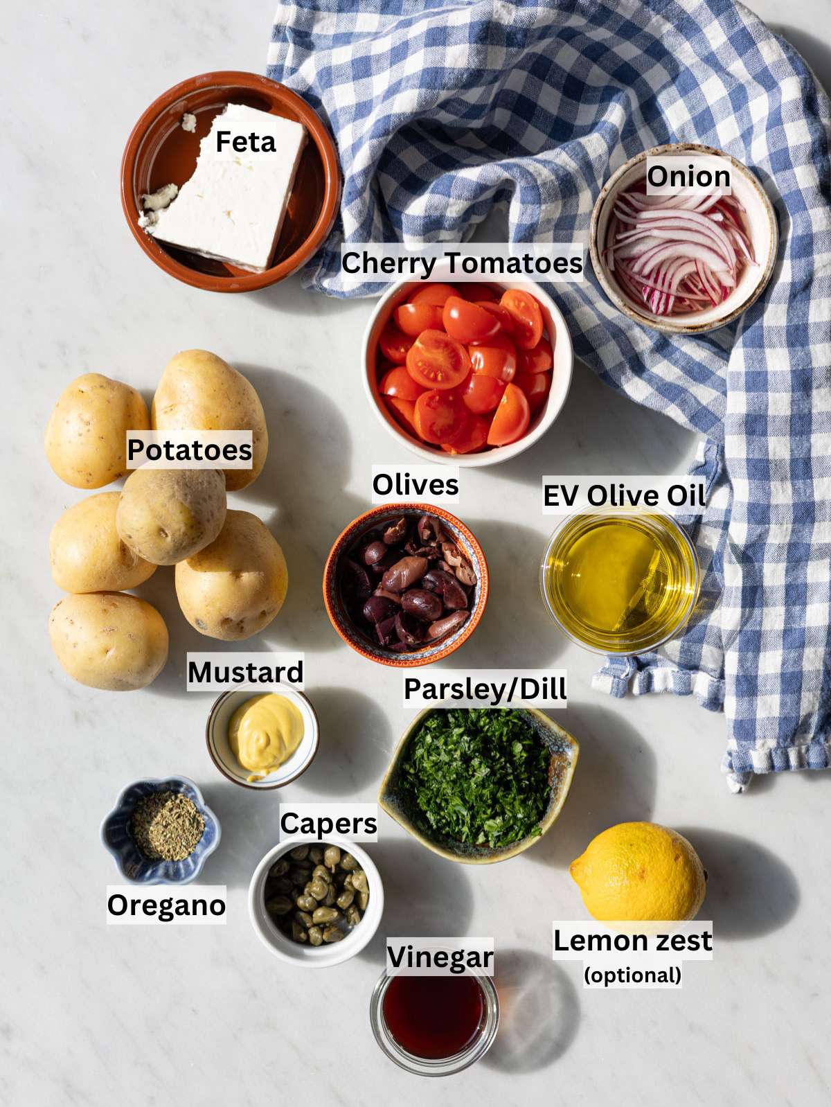 Ingredients for Greek potato salad arranged on marble table near window with natural light.