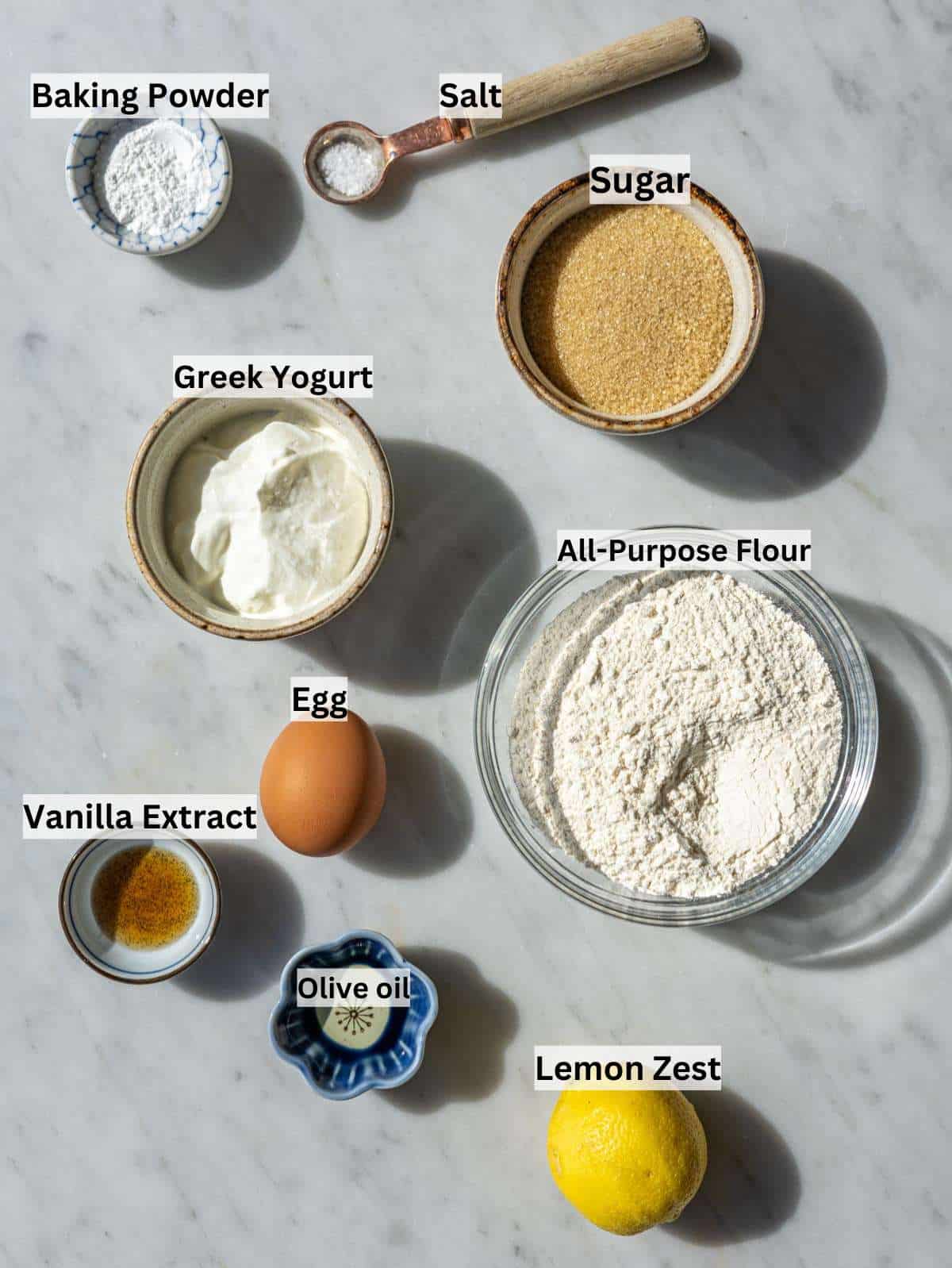 Ingredients for Greek yogurt cake donuts on marble surface in soft natural window light.