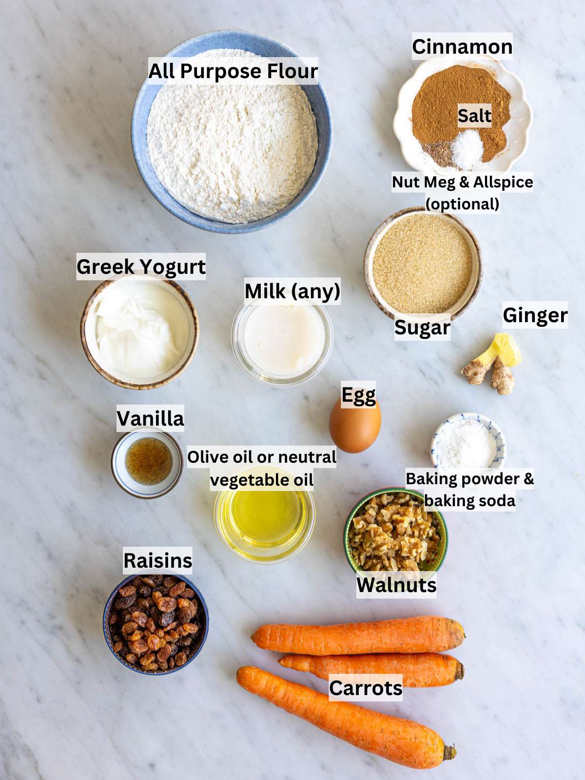 Ingredients for Greek yogurt carrot cake arranged on marble table in natural light.