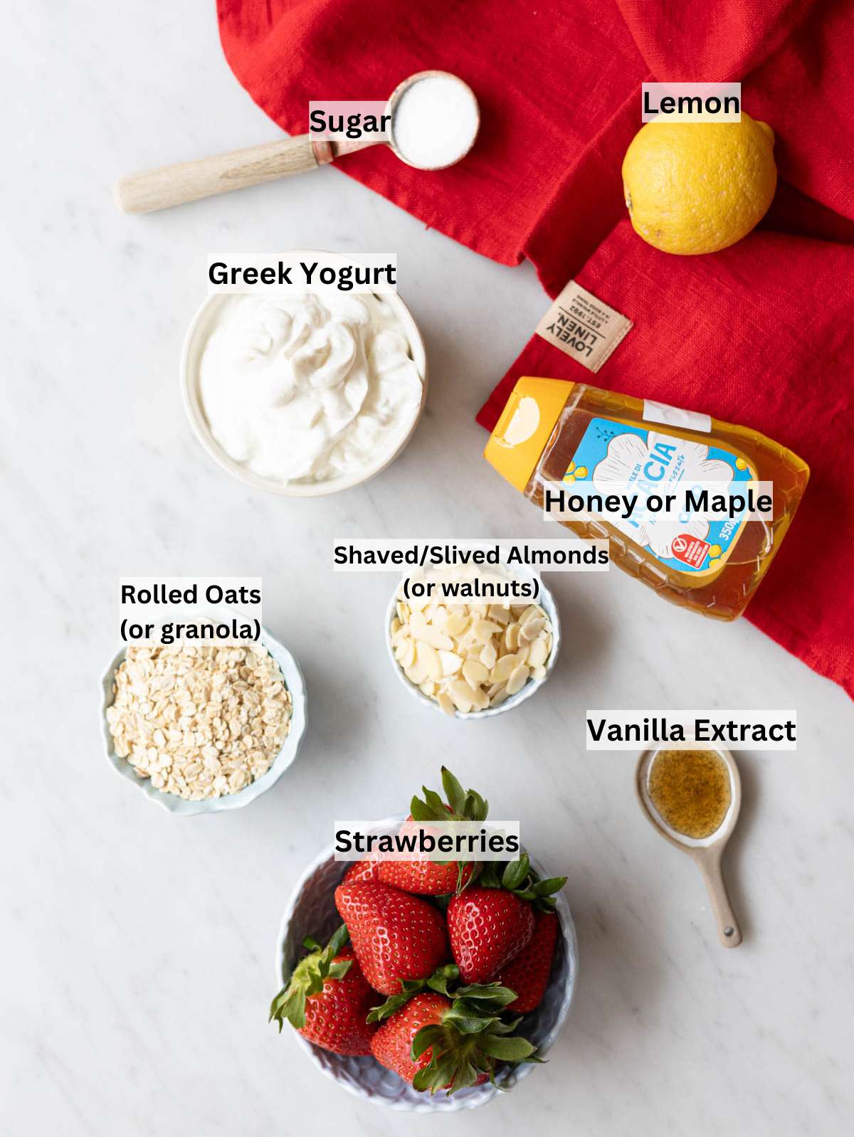 Ingredients for Greek yogurt parfait arranged on marble table near window light.