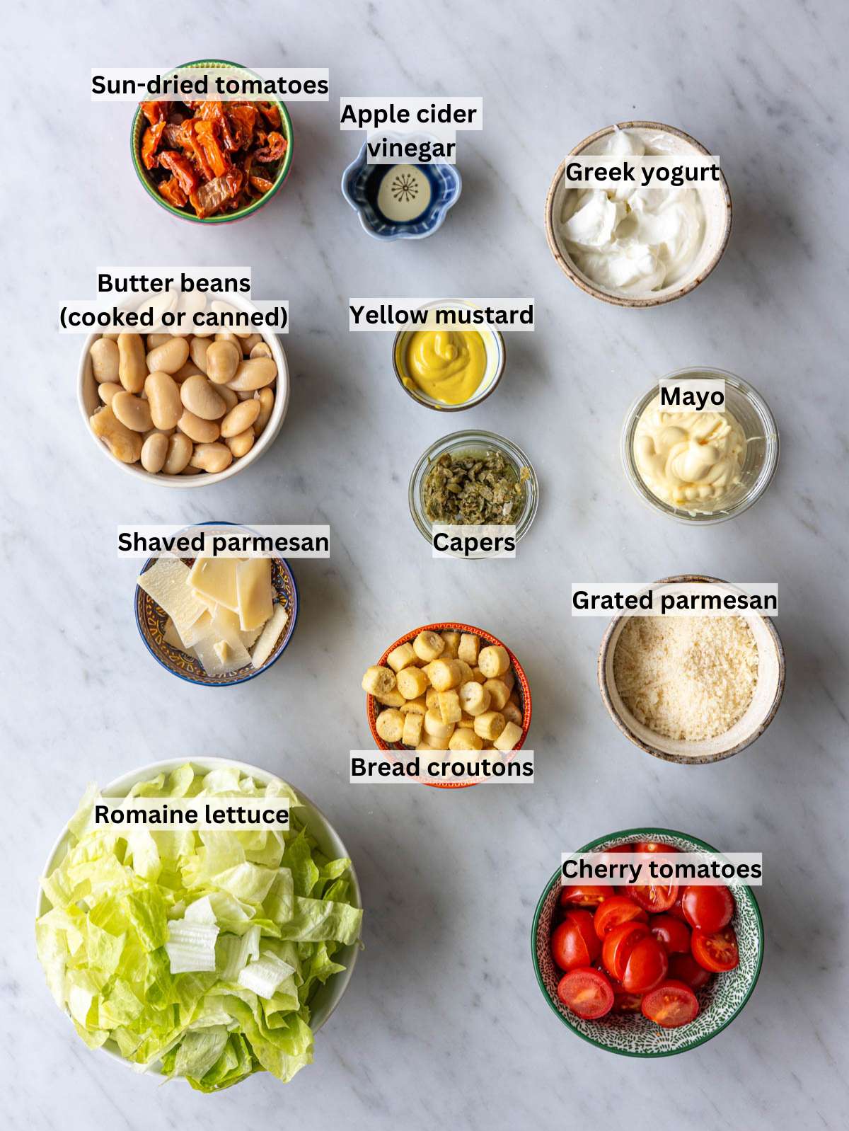 Ingredients for butter bean Caesar salad arranged on marble table in bright natural window light.