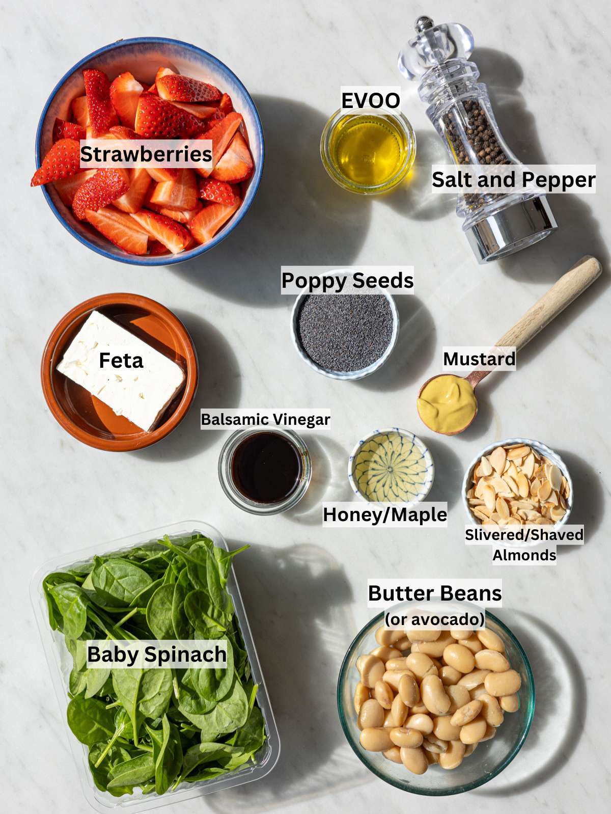 Ingredients for strawberry spinach salad arranged on marble table near window in soft natural light.