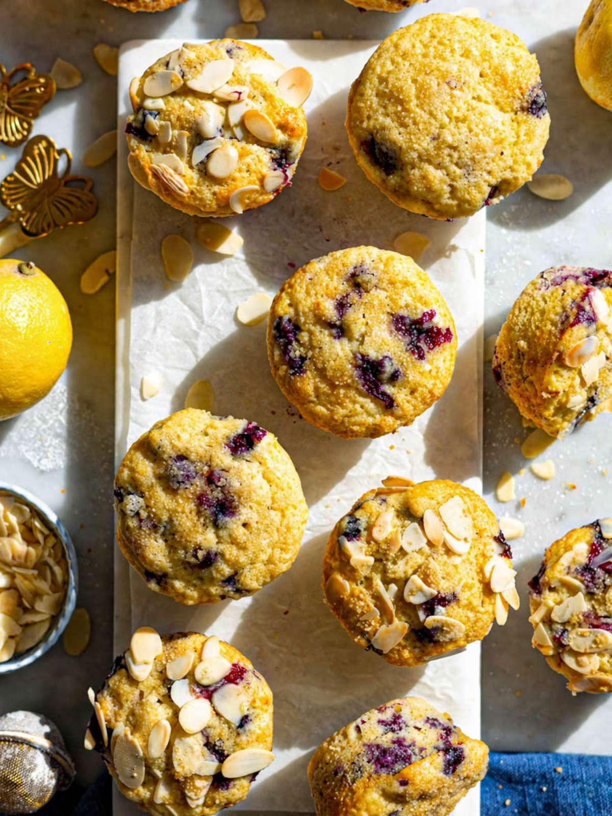 Lemon blueberry muffins on marble table near window with natural light and soft shadows.
