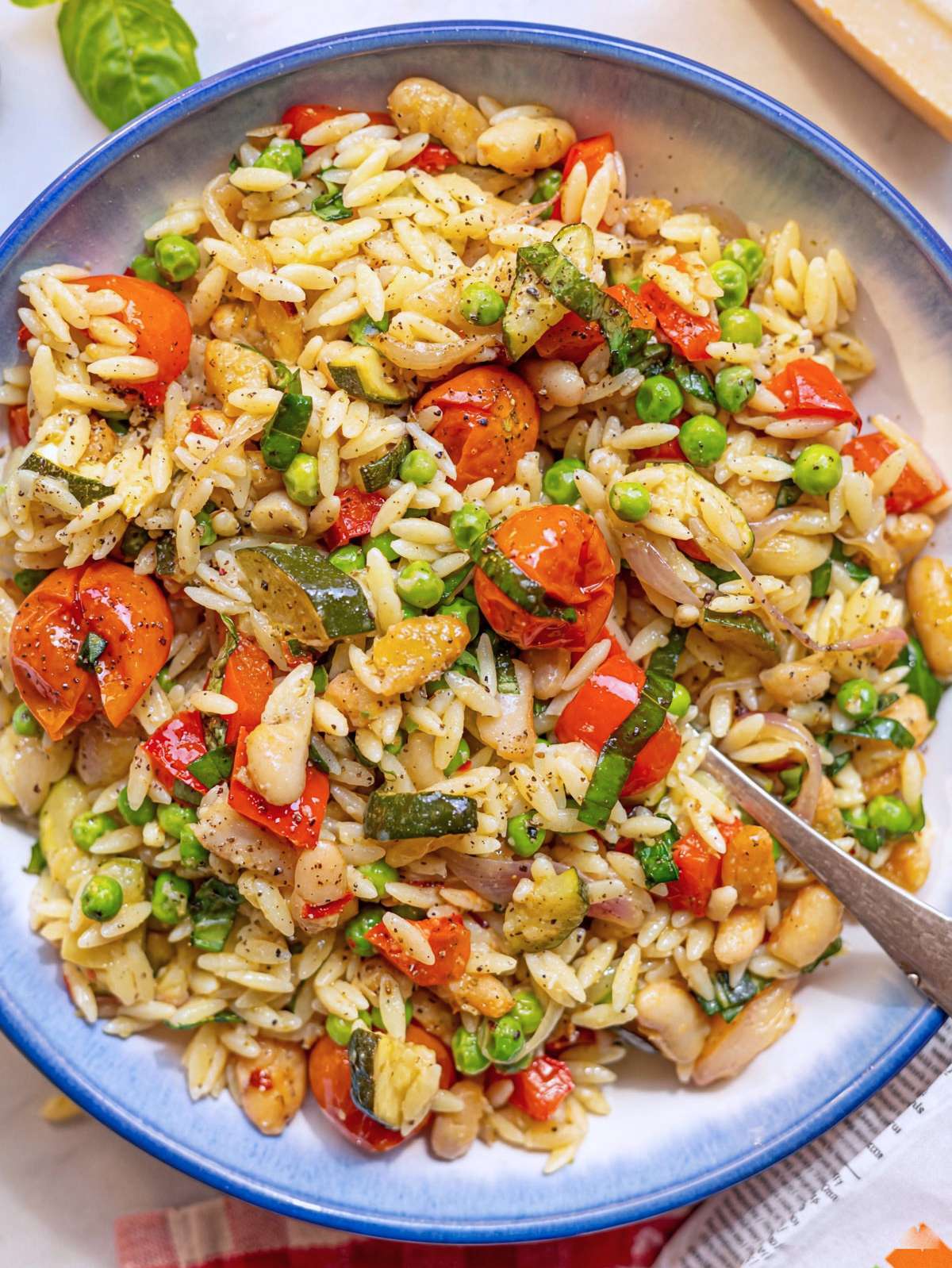 Orzo primavera tossed with roasted vegetables and parmesan in a bowl near window.