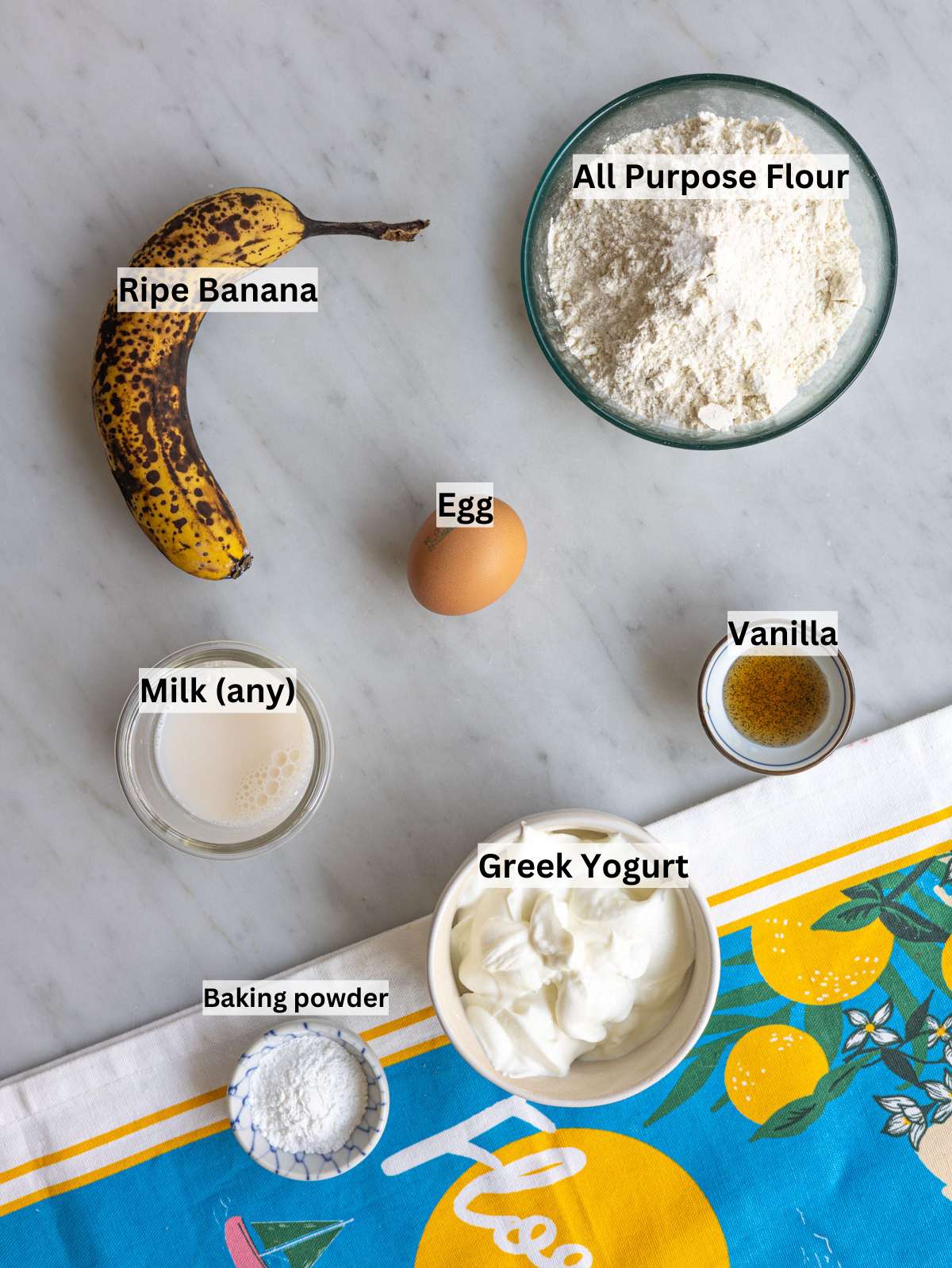 Ripe banana Greek yogurt egg flour and milk on marble table in natural light.