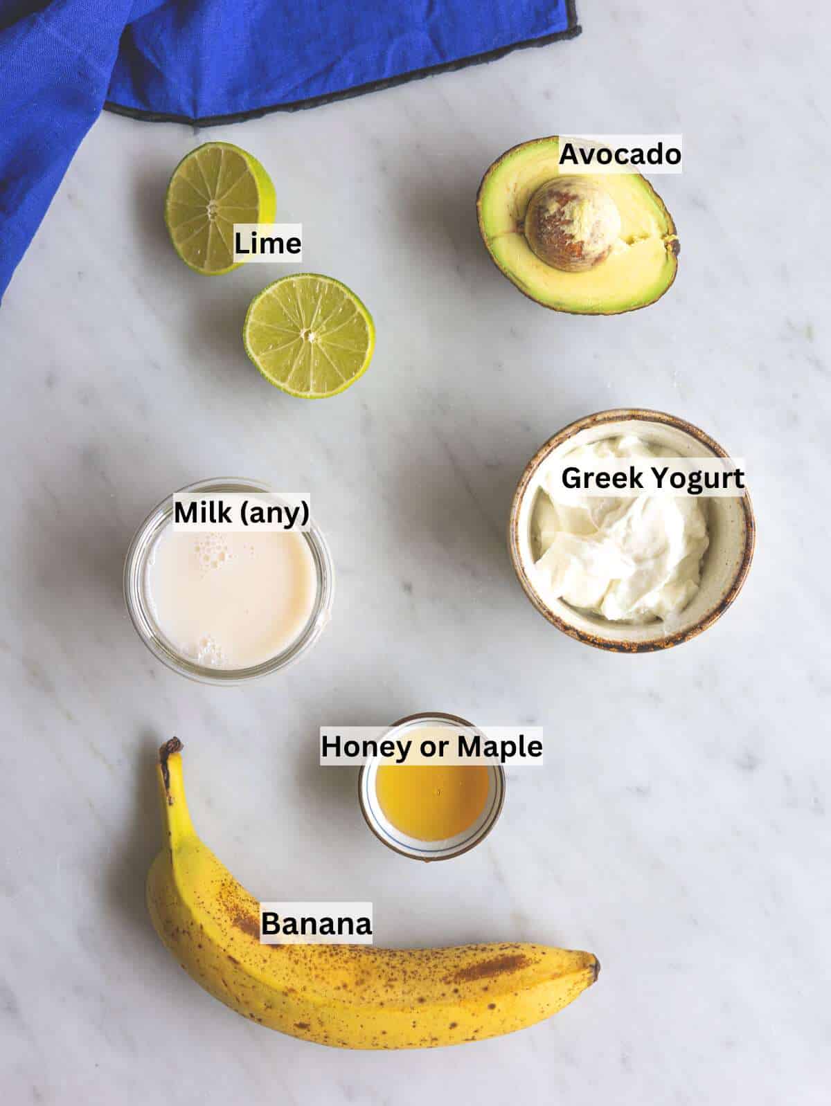 Ripe banana, avocado, Greek yogurt, and milk arranged on marble surface in soft light.