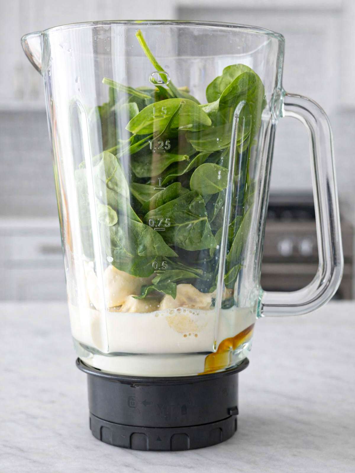 Spinach, banana, milk, and honey in blender jar ready to blend into green smoothie.