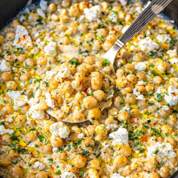 Spoon lifting creamy chickpeas from lemon skillet with yogurt sauce.