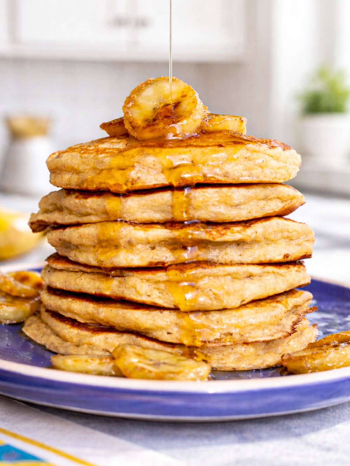 Stack of banana oatmeal pancakes with Greek yogurt topped with sautéed bananas and maple syrup.