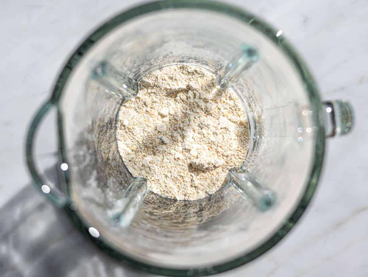 Step 1 Rolled oats blending into oat flour in a blender jar on marble countertop.