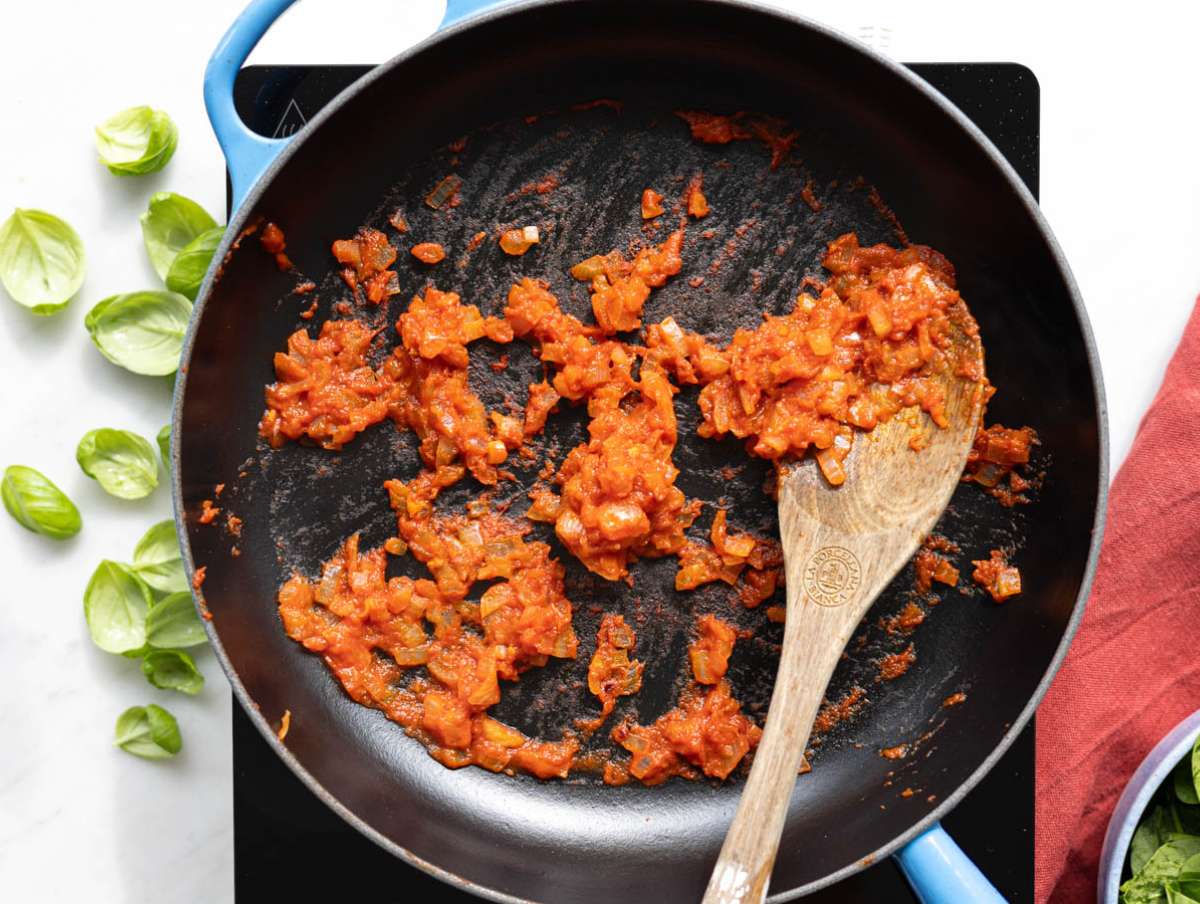 Step 1 Sautéing onions, garlic, and tomato paste in a skillet on a marble countertop background.
