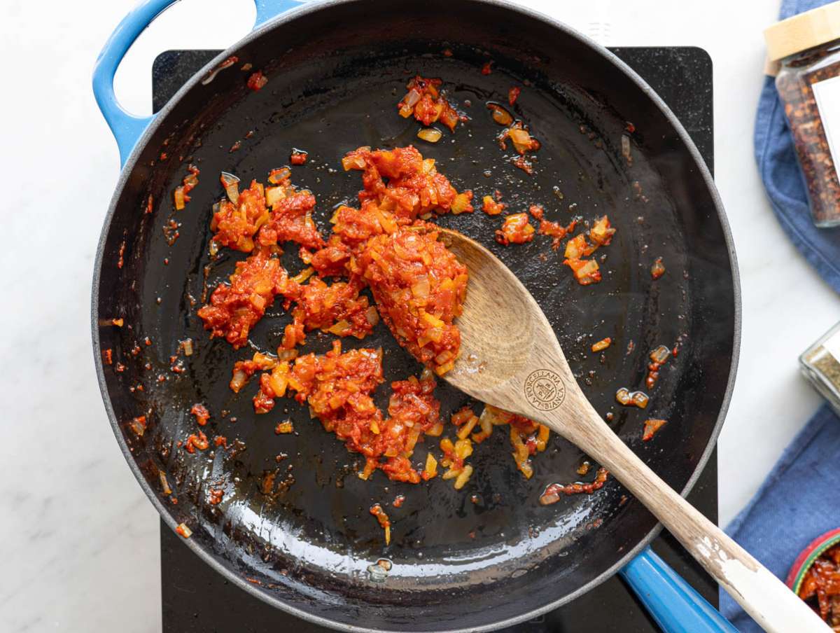 Step 1 Softened onions and toasted tomato paste simmering in a large skillet on a marble countertop.