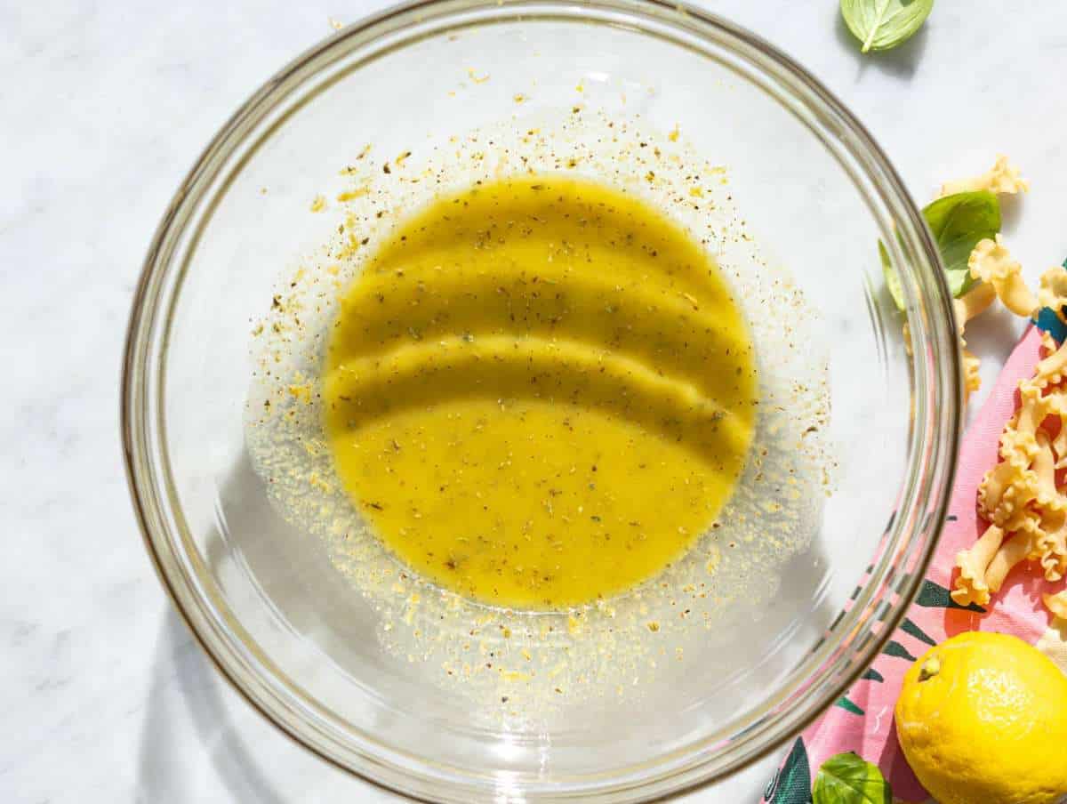 Step 1 Whisking lemon dressing in bowl on marble counter with natural daylight.