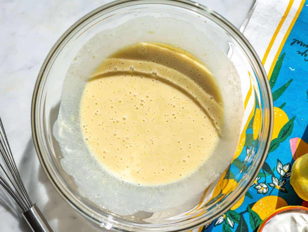 Step 1 Whisking yogurt egg and sugar mixture in glass bowl on marble surface.