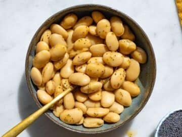 Step 2 Butter beans tossed with dressing in bowl with glossy coating and natural light.