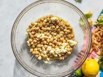Step 2 Chickpeas and feta marinating in lemon dressing in large bowl on marble surface.
