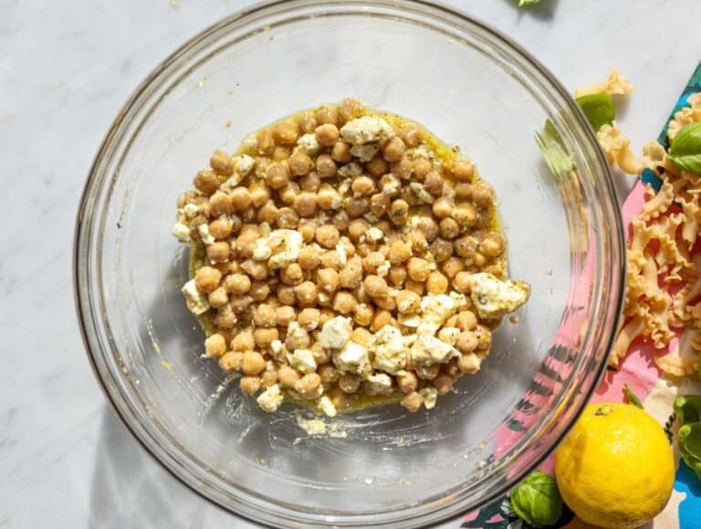 Step 2 Chickpeas and feta marinating in lemon dressing in large bowl on marble surface.