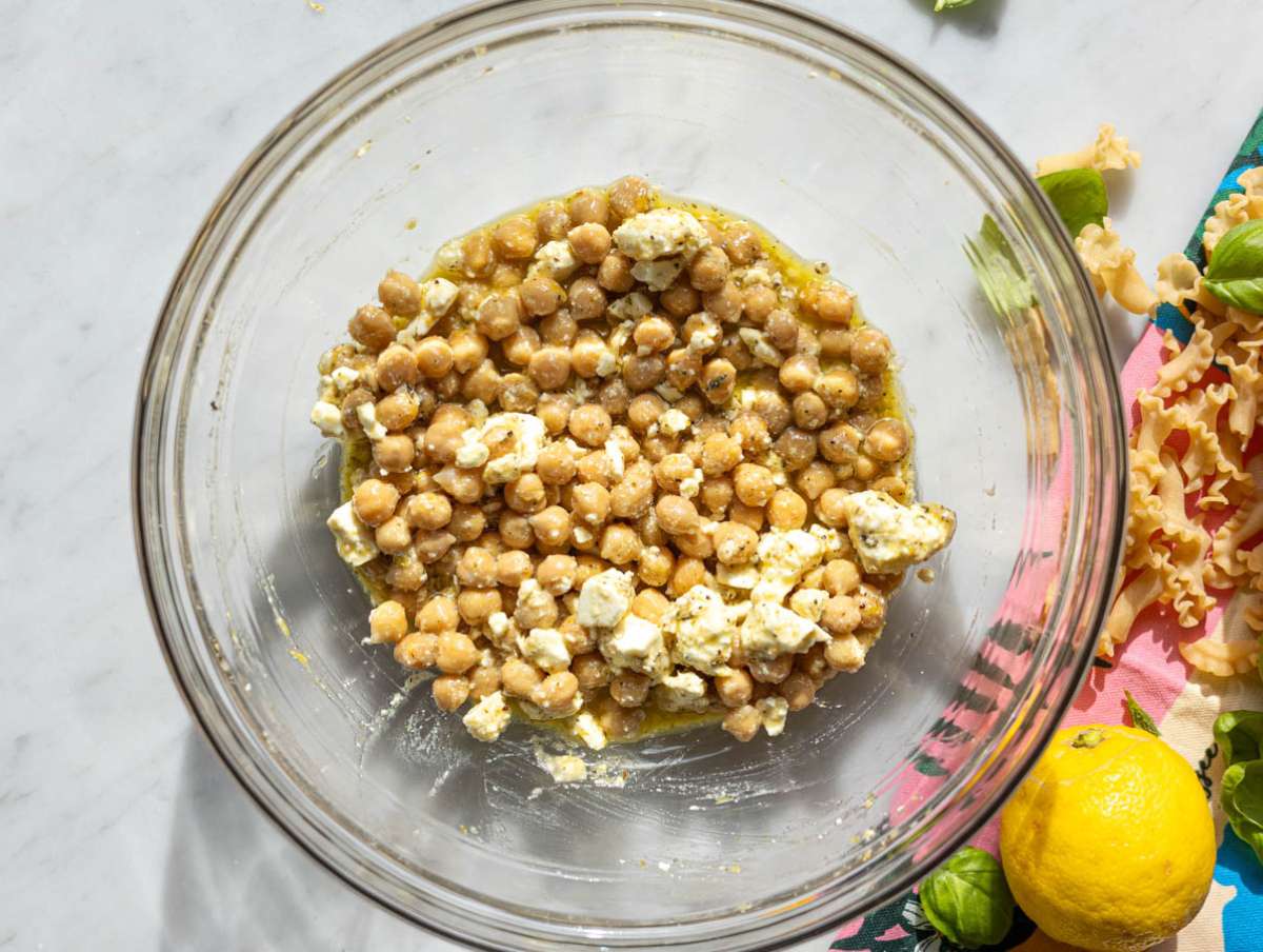 Step 2 Chickpeas and feta marinating in lemon dressing in large bowl on marble surface.