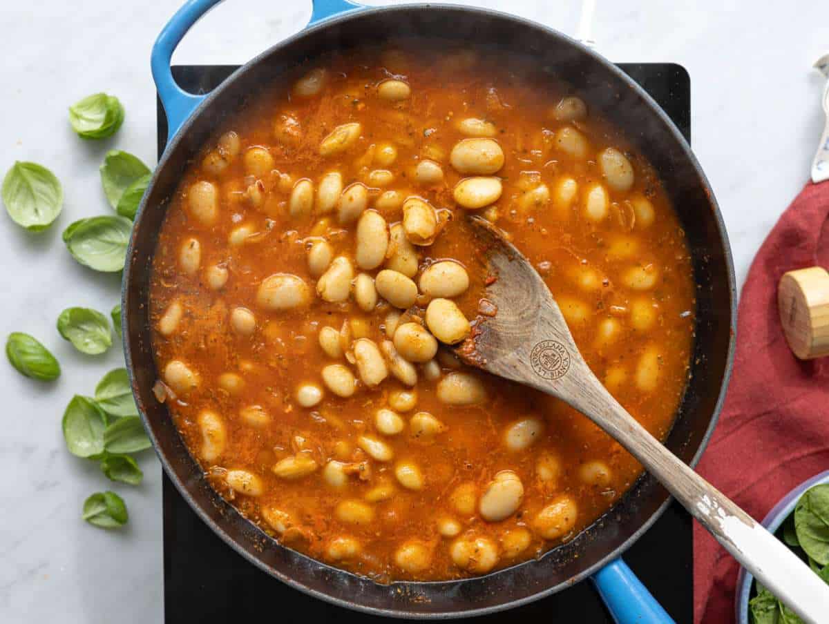 Step 2 Plump butter beans being tossed in a rich tomato and garlic base in a pan.