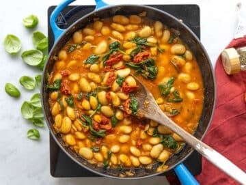 Step 3 Butter beans simmering in broth with sun-dried tomatoes and bright green spinach leaves.