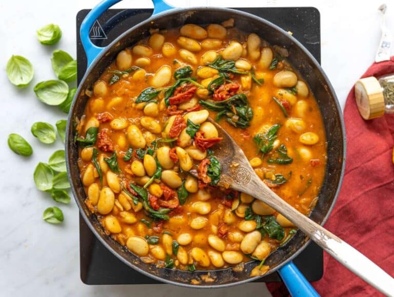 Step 3 Butter beans simmering in broth with sun-dried tomatoes and bright green spinach leaves.