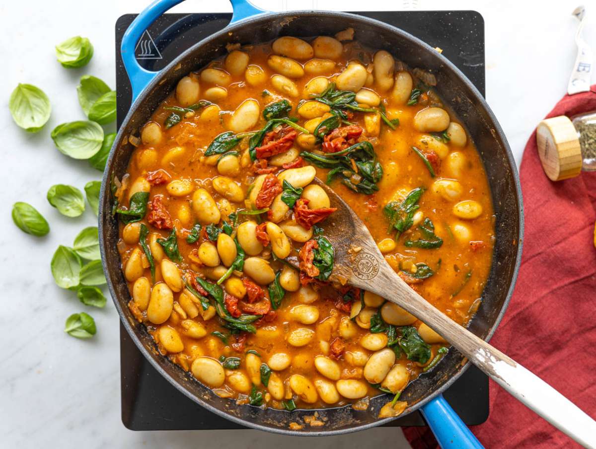 Step 3 Butter beans simmering in broth with sun-dried tomatoes and bright green spinach leaves.