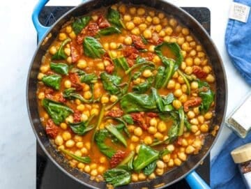Step 3 Fresh baby spinach and sliced sun-dried tomatoes being folded into a simmering chickpea mixture.