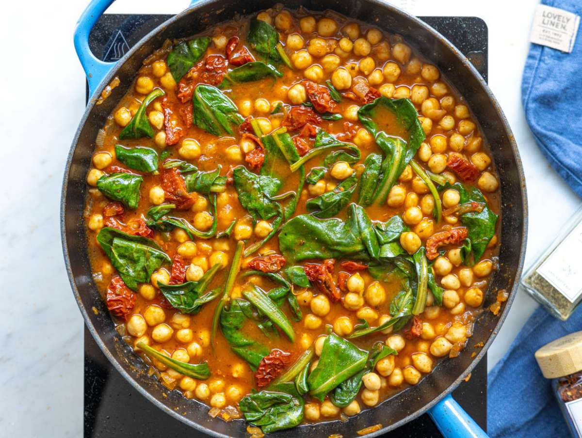 Step 3 Fresh baby spinach and sliced sun-dried tomatoes being folded into a simmering chickpea mixture.