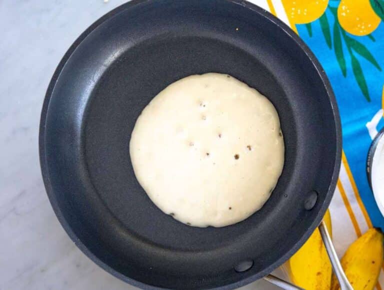 Step 3 Pancake batter cooking in skillet with bubbles forming and edges setting.