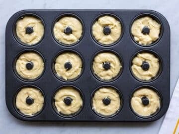 Step 3 Spoon filling donut pan with smooth batter on marble countertop.