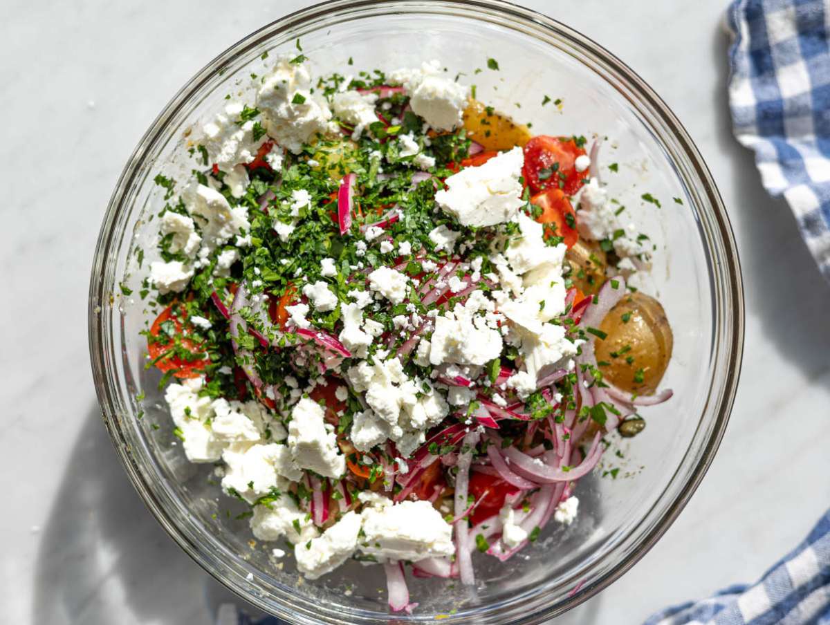Step 4 Potatoes mixed with tomatoes olives capers herbs and feta in a large bowl.
