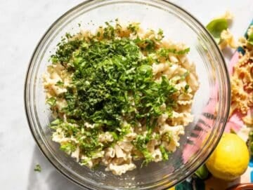 Step 4 Tossing pasta with chickpeas herbs and feta in large bowl on marble table.
