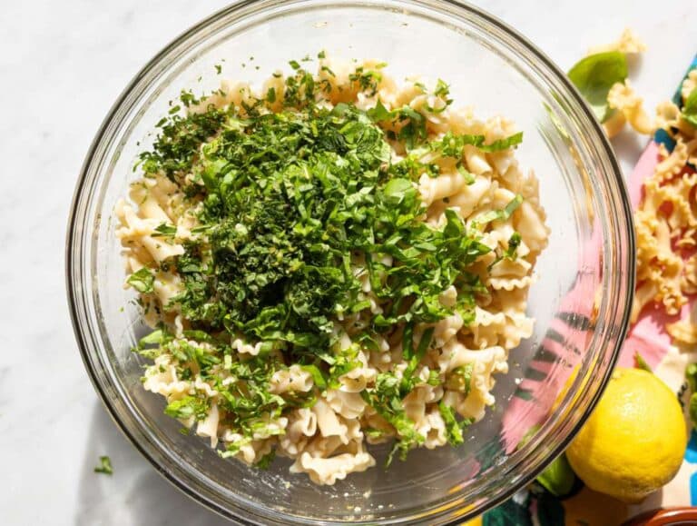 Step 4 Tossing pasta with chickpeas herbs and feta in large bowl on marble table.