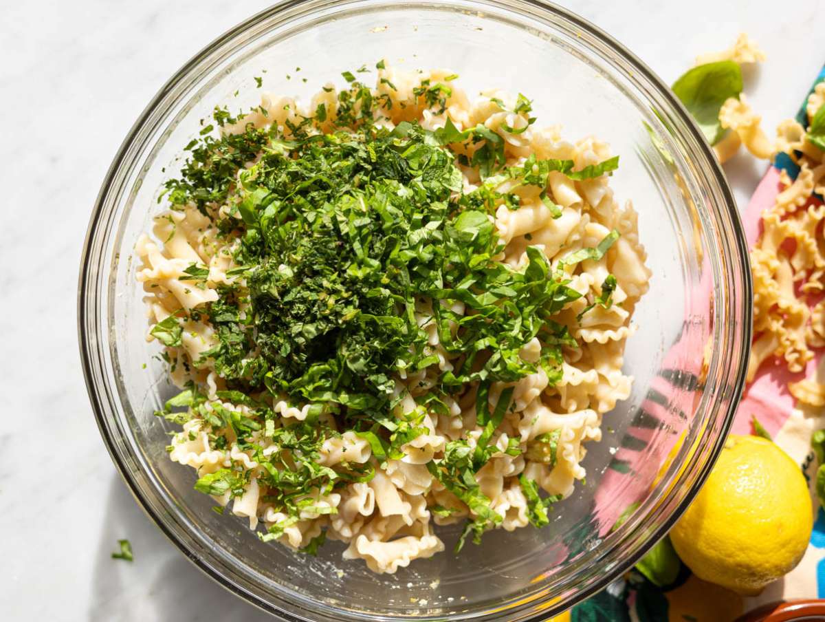 Step 4 Tossing pasta with chickpeas herbs and feta in large bowl on marble table.