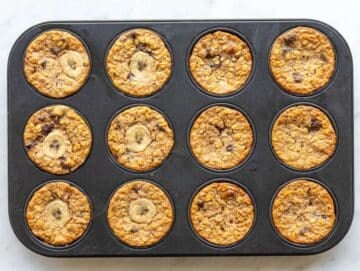 Step 5 Freshly baked banana baked oatmeal cups cooling in muffin pan on marble counter.