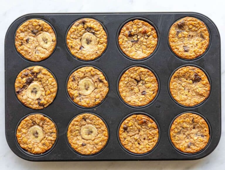 Step 5 Freshly baked banana baked oatmeal cups cooling in muffin pan on marble counter.