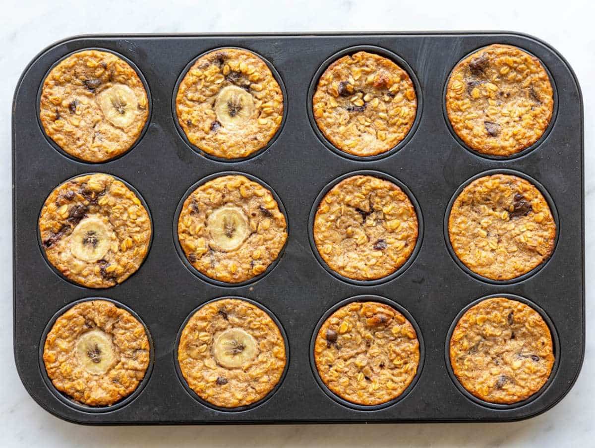Step 5 Freshly baked banana baked oatmeal cups cooling in muffin pan on marble counter.