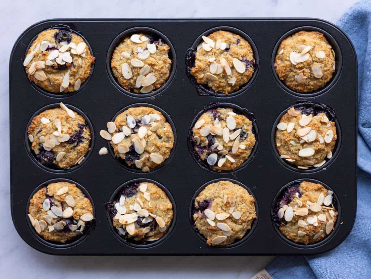 Step 5 Golden muffins topped with shaved almonds cooling on a marble surface.